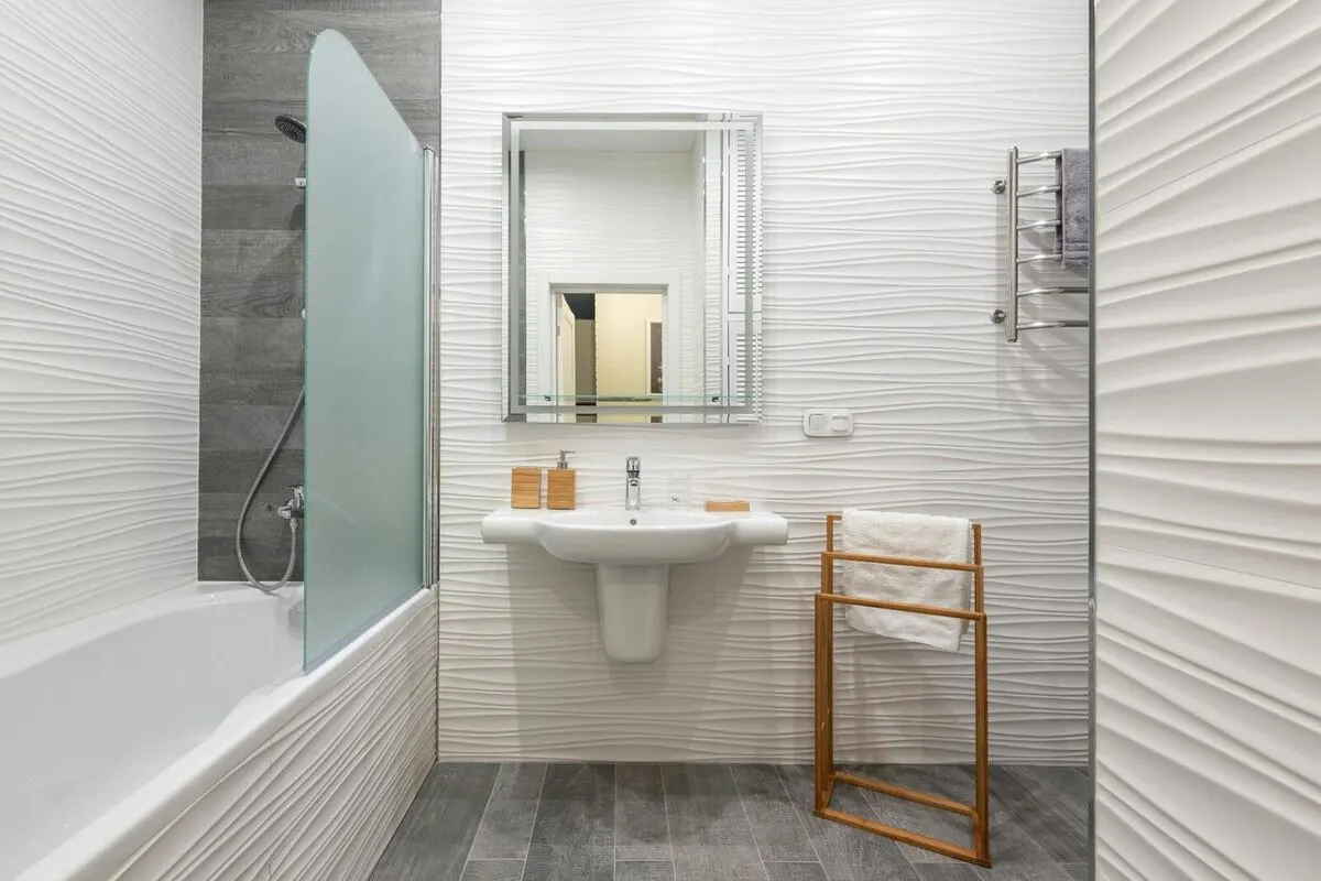 White 3D wave tile bathroom with wood look floor and frosted glass tub partition