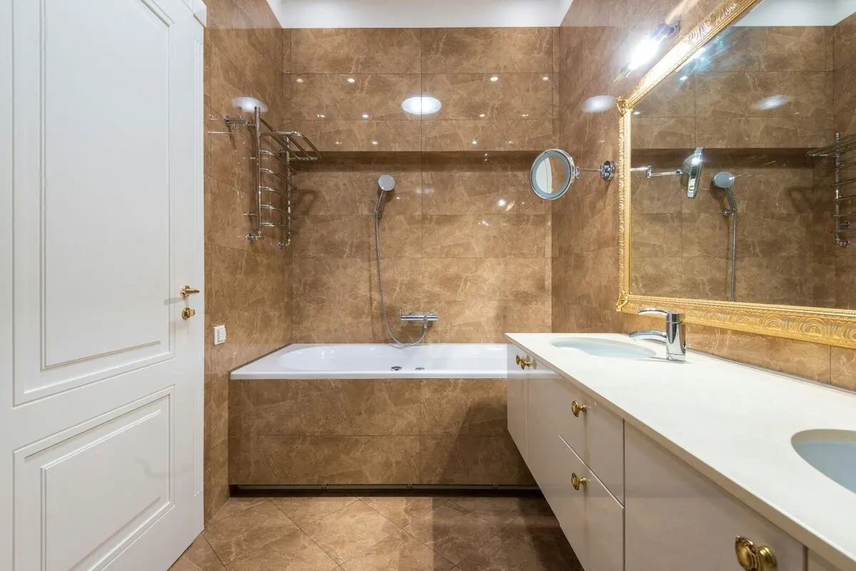 Polished brown marble bathroom with gold framed mirror and white vanity